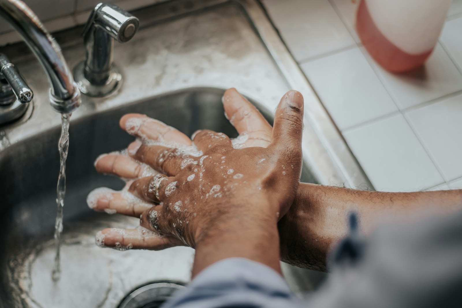 Persona lavándose las manos con agua y jabón en un lavabo.